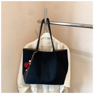 Detailed close-up of a large black tote bag with red fur ball charm on a beige suit