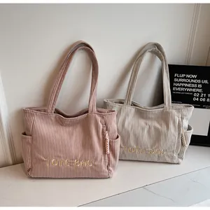 Macro shot of corduroy tote bags in pink and beige featuring bold TOTE BAG embroidery