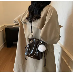 Sac seau en cuir verni marron foncé avec chaîne dorée et pompon blanc sur un modèle