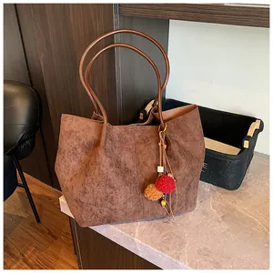 Detail of a large brown suede tote bag with colorful pompom charms on marble surface