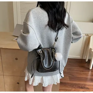 Détail du sac seau noir avec cordon de serrage, texture cuir PU et pompon blanc en peluche