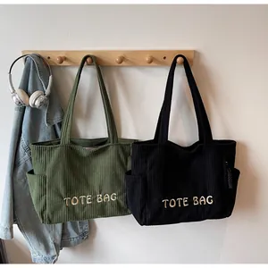 Detail of corduroy tote bags in army green and black with TOTE BAG white embroidery