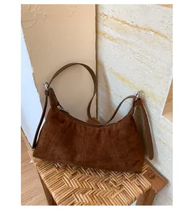 Close-up of brown suede hobo bag with adjustable strap on a woven rattan stool