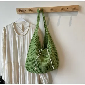Close-up of green hollow crochet tote bag with white drawstring on a wooden hanger
