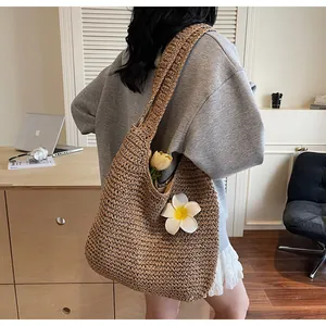 Détail d'un grand sac cabas tissé en paille marron foncé avec une fleur de frangipanier
