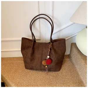 Detail of dark brown suede tote bag with plush pom-pom tassel on a textured stone step