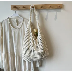 Detail of a beige crochet knit tote bag with large hollow mesh texture hanging on wood