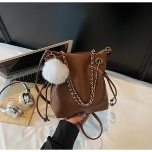 Détail du sac seau marron foncé avec chaîne dorée, cordon de serrage et pompon en peluche