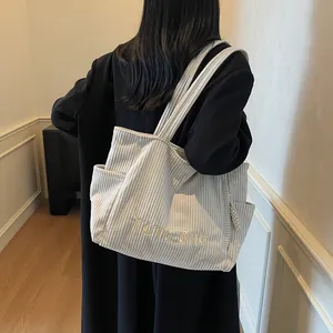 Minimalist beige corduroy tote bag with yellow embroidery on a black winter coat