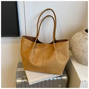 Detail view of large mustard suede tote bag with vertical stitching on travel suitcase