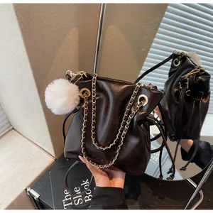 Détail du sac seau marron foncé avec chaîne dorée et pompon blanc en peluche