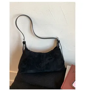 Macro shot of black suede baguette bag showing the matte texture and slim leather strap