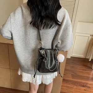 Sac seau noir à cordon chic avec chaîne dorée et pompon blanc porté par un mannequin