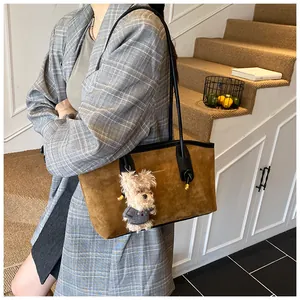 Détail du sac à bandoulière en daim caramel avec bandoulière noire et breloque ours