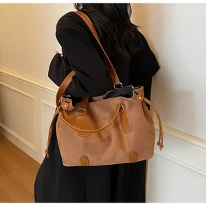 Detail of a large tan suede tote bag with leather straps on a model in a French style room