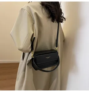 Detalle de un bolso bandolera negro estructurado con letras doradas y ganchos