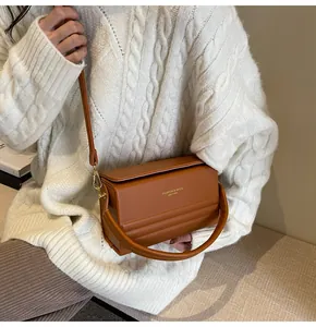 Detalle del bolso de caja marrón con texto dorado y asa redonda rígida de diseño único