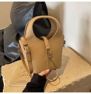 Détail d'un sac seau en cuir litchi abricot avec breloque nœud doré et poignée anneau