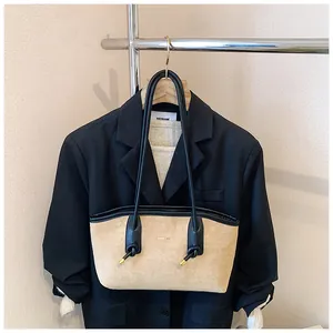 Détail du sac cabas en daim beige avec bordures en cuir noir sur un support en métal