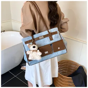 Detail of denim tote bag with leather straps and plush bear charm on model's shoulder