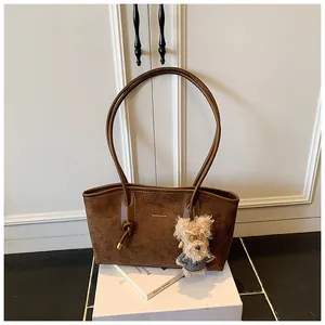 Détail d'un sac bandoulière en daim marron foncé avec logo et charme de chien