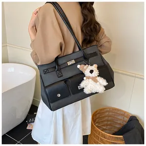 Close-up of black leather tote bag with silver twist locks and a plush bear pendant
