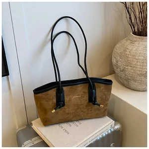 Détails d'un sac cabas en daim marron avec anses en cuir noir et finitions dorées en métal