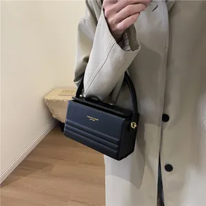 Bolso de mano tipo caja negro con letras doradas y herrajes llevado por una modelo