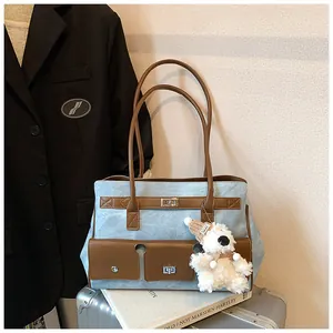 Detail view of denim texture tote bag with brown leather handles and plush bear charm