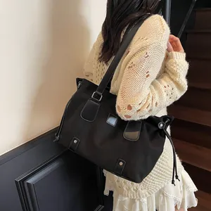 Black canvas tote bag with leather straps shown on shoulder in a lifestyle setting
