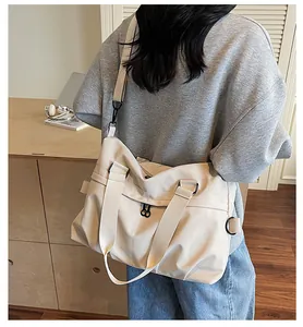 Detail of a large beige nylon crossbody bag featuring black adjustable straps and zippers