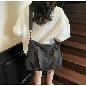 Rear view of a model carrying the large black nylon tote bag with a wide shoulder strap