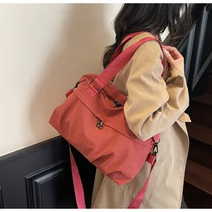 Model wearing a large brick red nylon crossbody travel bag on a stylish staircase