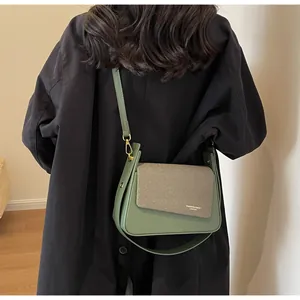 Detail view of khaki textile flap with logo and dark green leather on a crossbody bag
