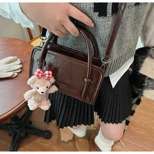 Detail view of dark brown glossy leather handbag with a plush bear charm on a wood table