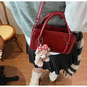 Detail of burgundy glossy handbag with plush bear charm and adjustable shoulder strap