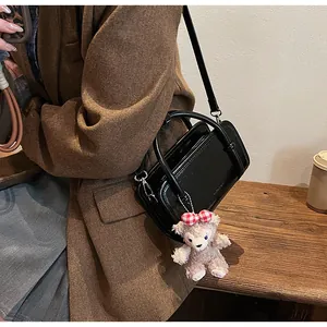 Detail of black glossy handbag with a plush bear charm worn with a stylish autumn blazer