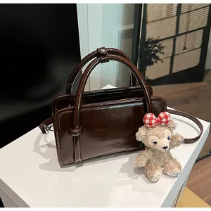 Detailed view of deep brown polished leather handbag with handle and CLEAMOR logo