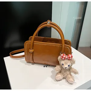 Detail of caramel brown matte leather handbag with plush bear charm and white logo