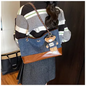 Detailed shot of large denim tote bag with chain strap and teddy bear charm accessory
