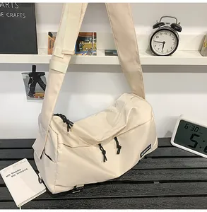 Detailed close-up of cream nylon crossbody bag featuring black zipper pulls and wide strap