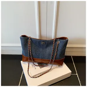 Detail of color-block denim tote bag showing vintage leather trim and metal chain strap