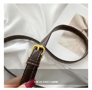 Detalle de correa ajustable de cuero marrón oscuro con hebilla dorada y costuras blancas