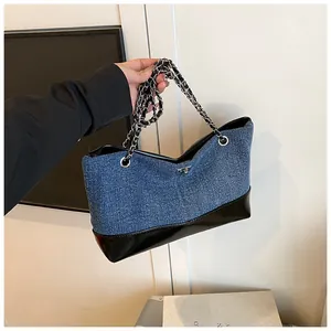 Detail of blue denim tote bag with black faux leather base and silver chain strap handle