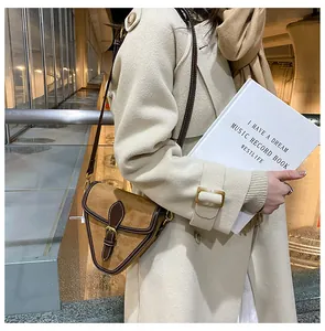Detalle de bolso bandolera triangular de ante con una gabardina color beige clásica