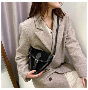 Detalle de bolso bandolera triangular en cuero mate negro con hebilla dorada y costuras