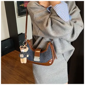 Detail of denim and brown leather crescent bag with bear charm worn by a model