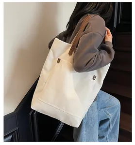 Large cream canvas tote bag with brown leather straps shown on a shoulder in a modern setting