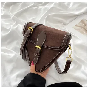 Detalle de bolso triangular marrón oscuro en ante con hebilla dorada y costuras blancas