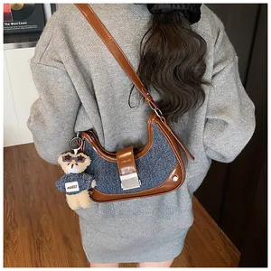 Detail of denim crescent bag with brown leather trim and a cute teddy bear pendant charm